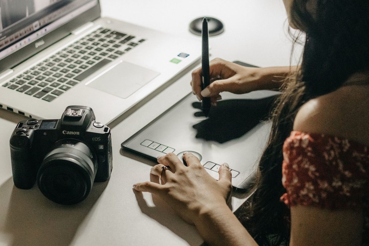 Close-up of a designer using a graphics tablet to create digital art alongside a laptop.