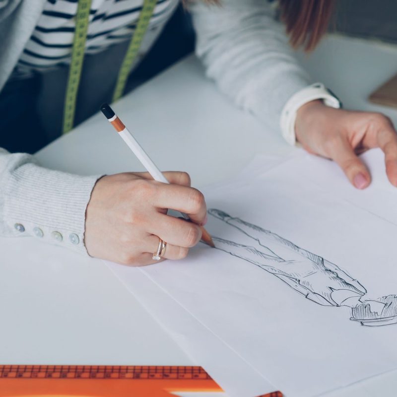 Fashion designer drawing sketches on paper, focusing on creativity and design.