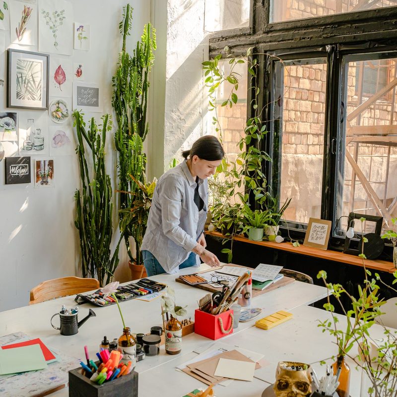 Designer working at a desk with sketches, pens, and plants in a bright studio.